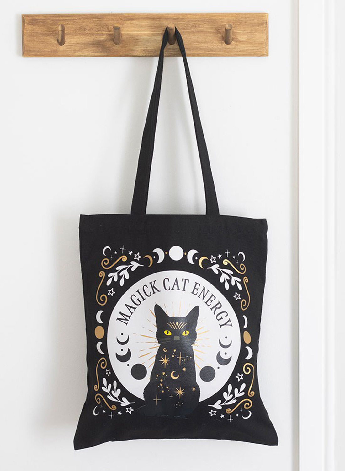 Black Magick Cat Energy Tote Bag – schwarze Stofftasche aus Polyester mit Katzenmotiven, gelben Augen, Mondphasen und Sternen. Abmessungen 38,5 × 33,8 cm.